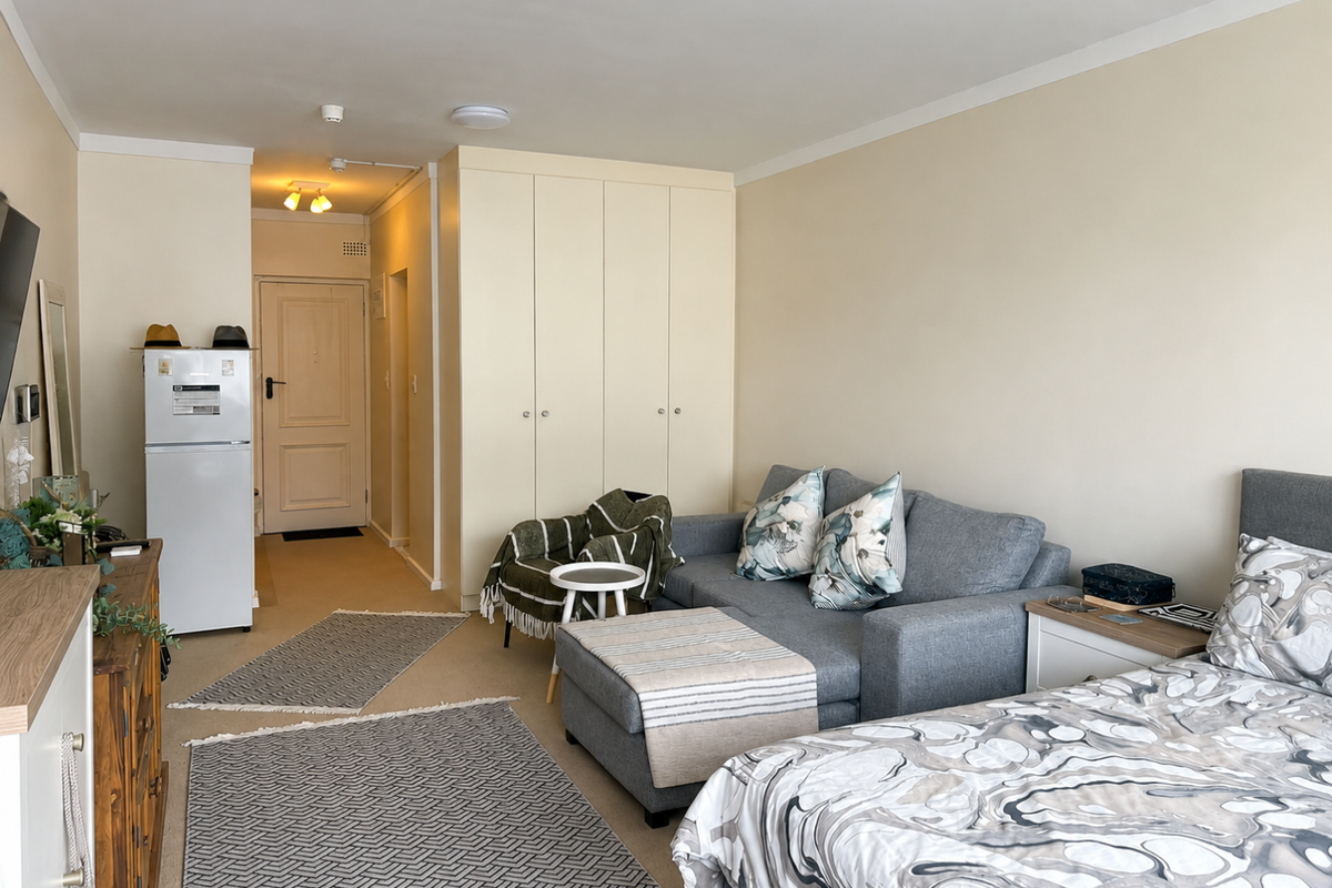 An open-plan studio apartment featuring neutral walls, carpeted flooring, and a large built-in wardrobe providing ample storage space.