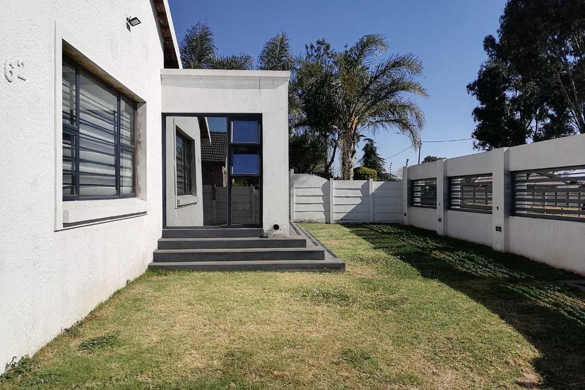 A rear exterior view of the property featuring a small lawn, concrete boundary wall, and modern aluminium-framed glass entrance.