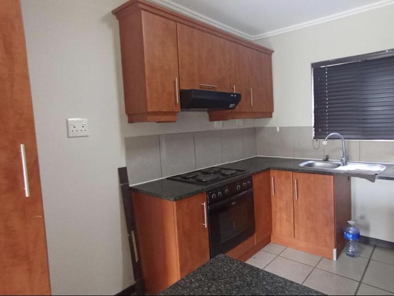 A functional kitchen featuring wood-finish cabinetry, granite countertops, a built-in oven with hob, and a tiled backsplash.