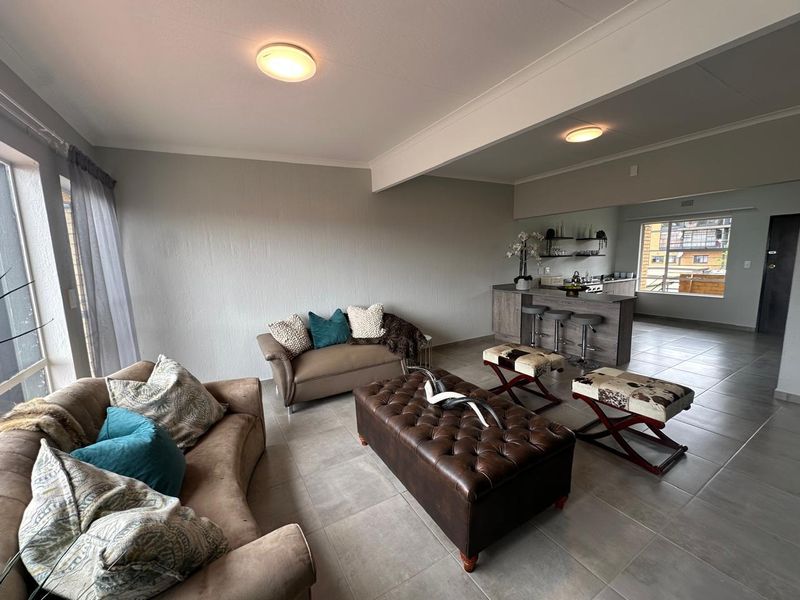 Spacious open-plan living area featuring tiled flooring, a central kitchen island with breakfast bar seating, and neutral wall finishes.