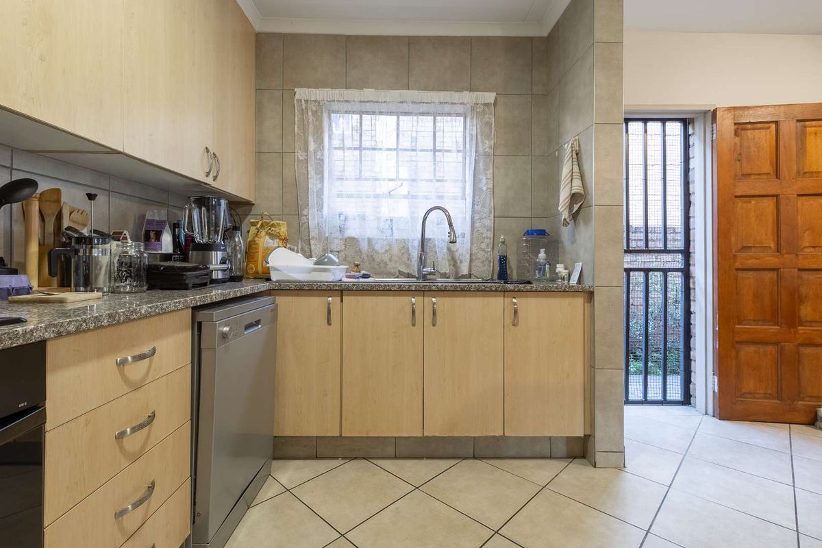 A functional kitchen featuring light wood cabinetry, granite countertops, tiled backsplash, and a stainless steel sink, with direct access to an exterior door.