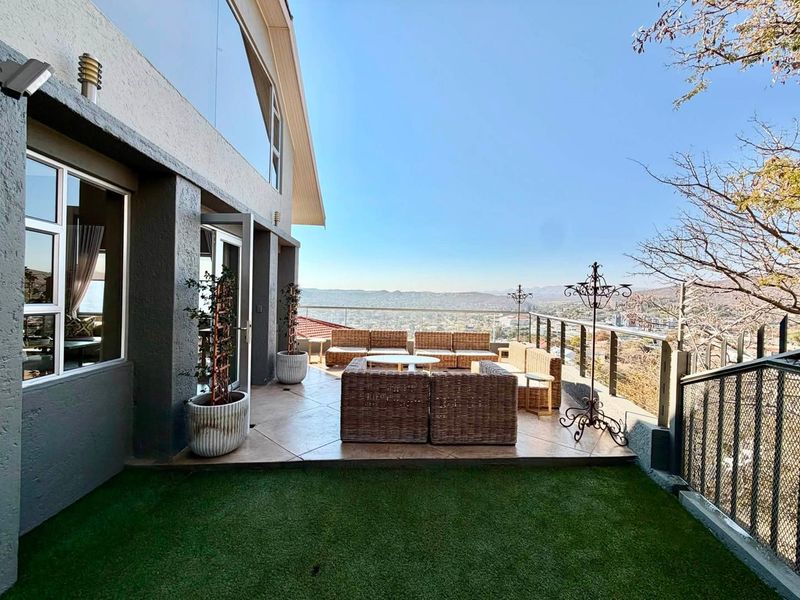 Spacious elevated patio featuring tiled flooring, a modern glass balustrade, and expansive panoramic views of the surrounding landscape.