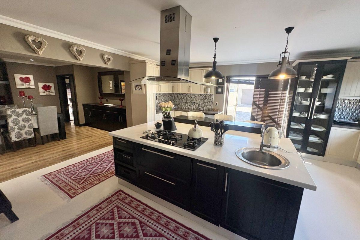 Modern kitchen featuring a central island with gas hob, stainless steel extractor fan, integrated sink, and ample dark cabinetry with glass display units.