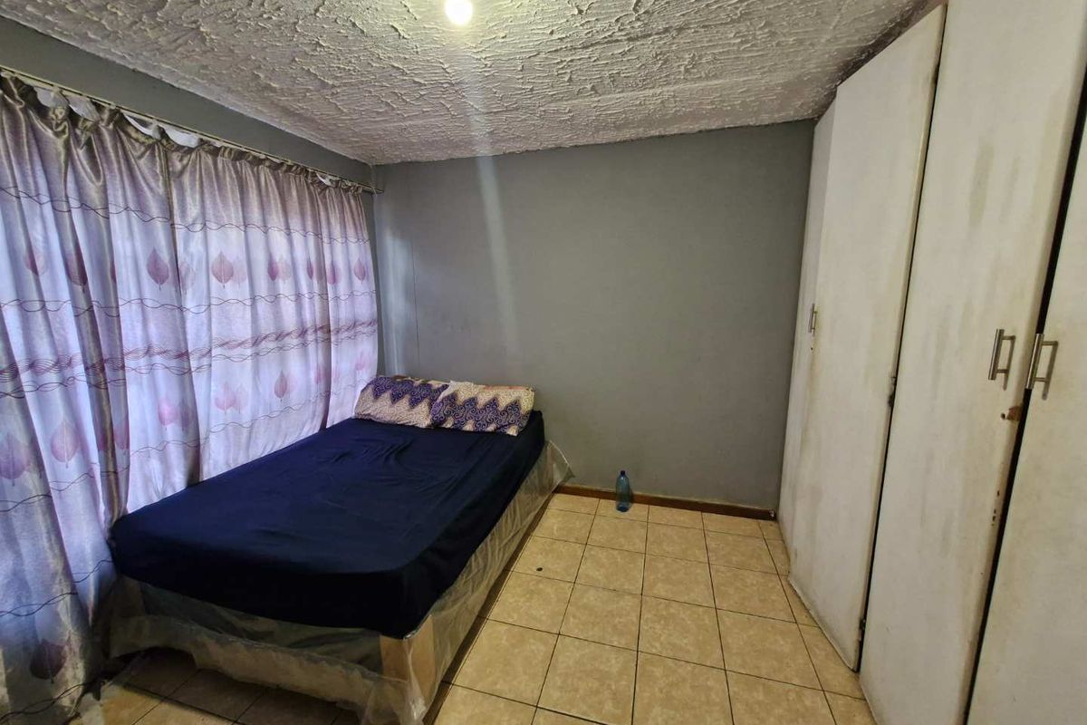 A bedroom featuring tiled flooring, built-in wardrobes, and a textured ceiling finish, offering a functional space in need of cosmetic updates.