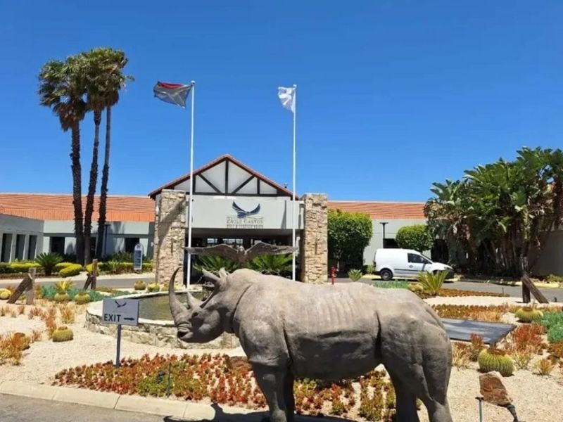 Front entrance view of the estate clubhouse featuring stone facade detailing, landscaped gardens, and a prominent rhino sculpture.