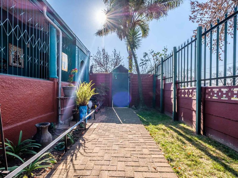 A paved side walkway leading to a rear garden area, featuring secure perimeter fencing and security bars on the building exterior.