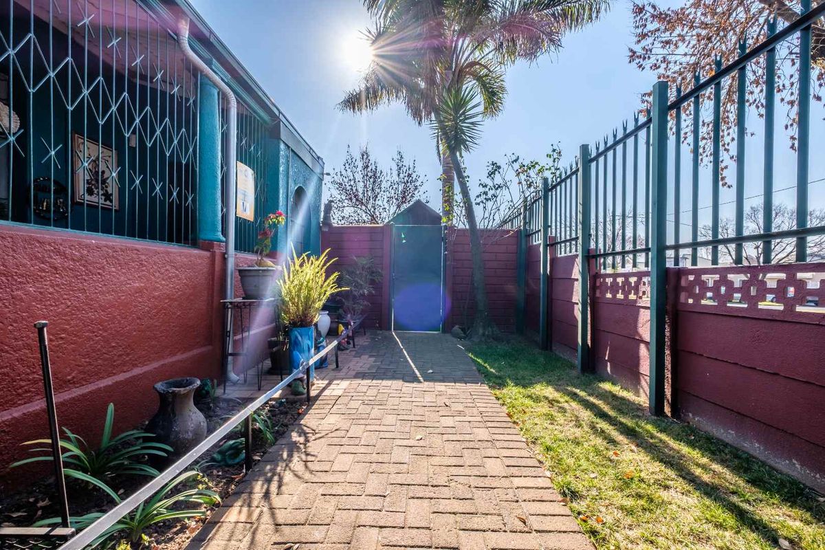 A paved side walkway leading to a rear garden area, featuring secure perimeter fencing and security bars on the building exterior.