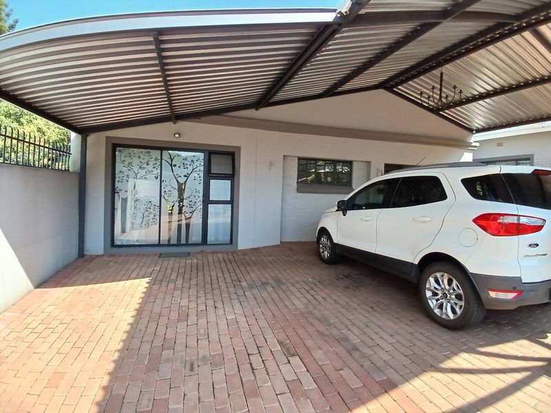 Front exterior view of the cottage featuring a covered carport, brick paved driveway, and a modern sliding glass entrance door.