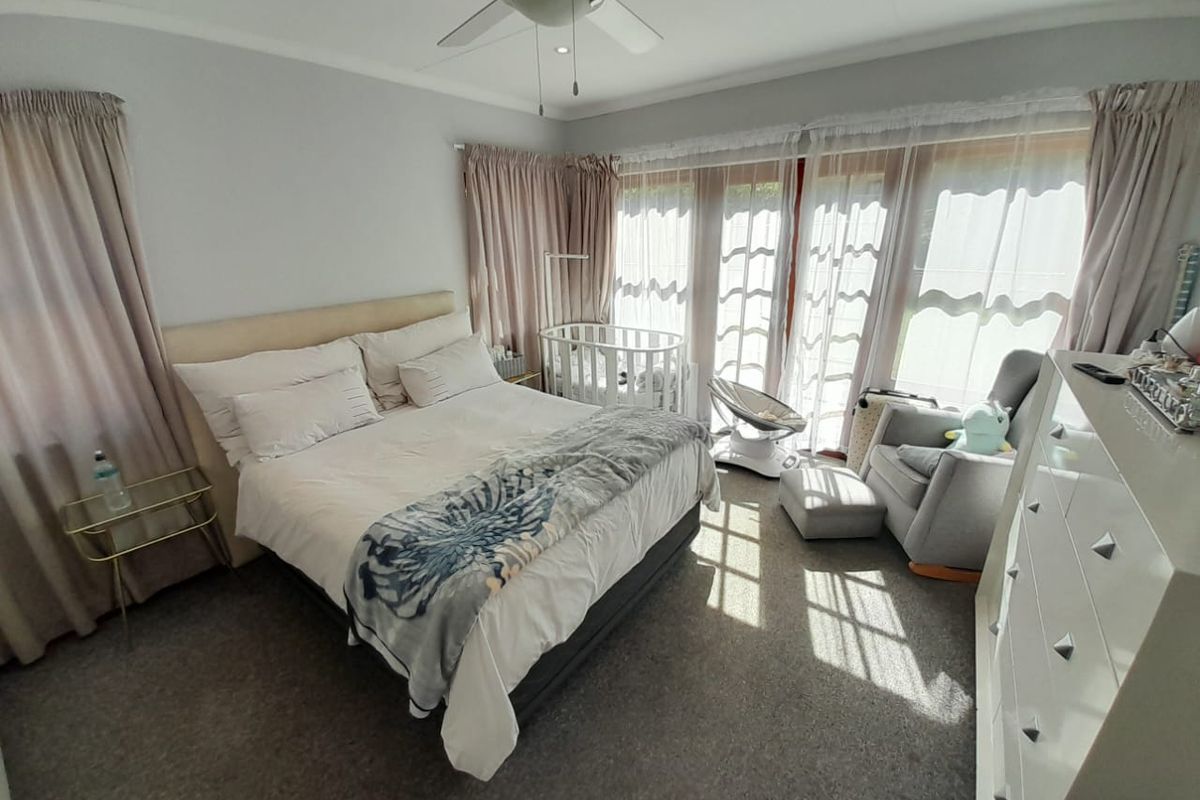 A bright and spacious bedroom featuring neutral carpeting, a ceiling fan, and large glass sliding doors that provide ample natural light.