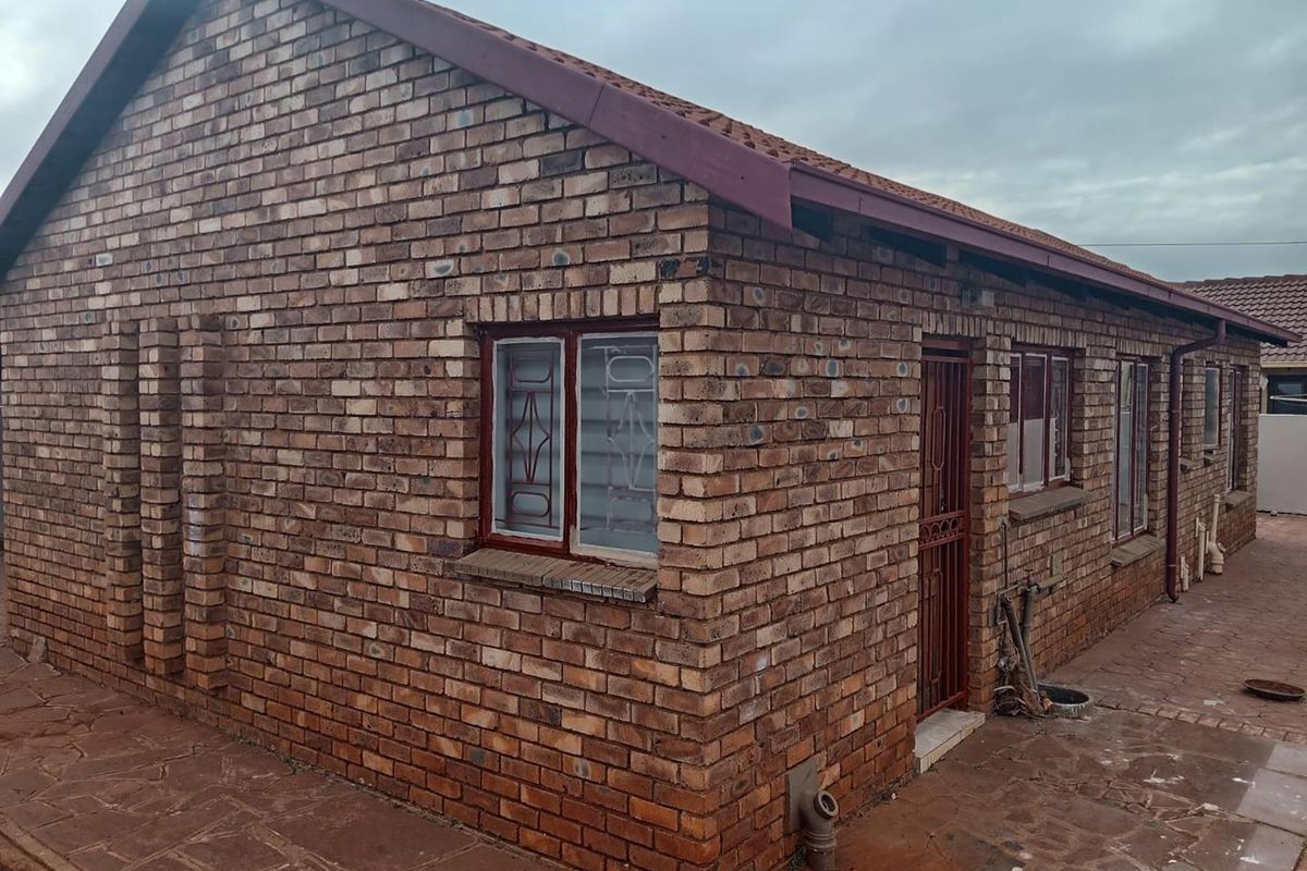 A side view of a face-brick house featuring metal security window bars, a security gate, and paved exterior surrounds.