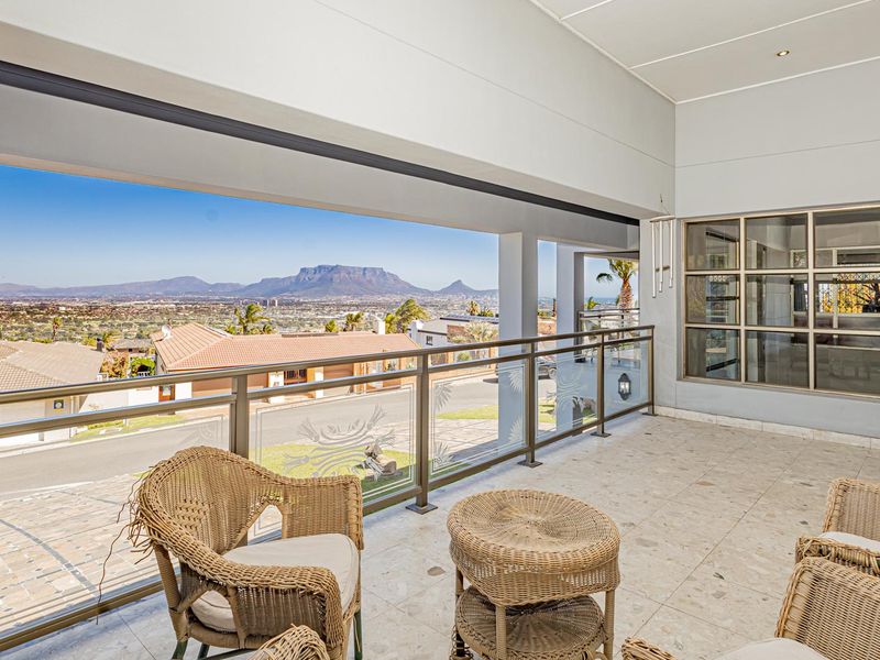 Spacious covered balcony featuring tiled flooring, a modern glass balustrade, and expansive views of the surrounding landscape and mountains.