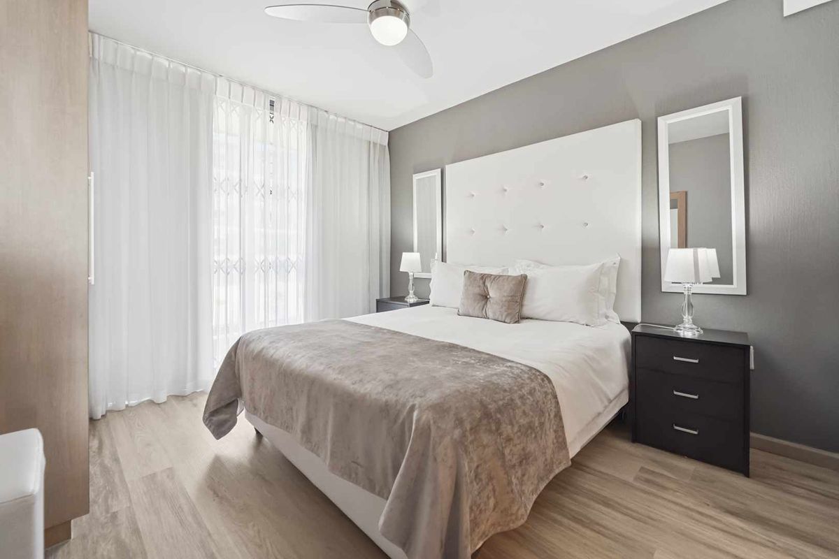 A well-maintained bedroom featuring light wood-look flooring, a ceiling fan, and neutral grey accent wall.