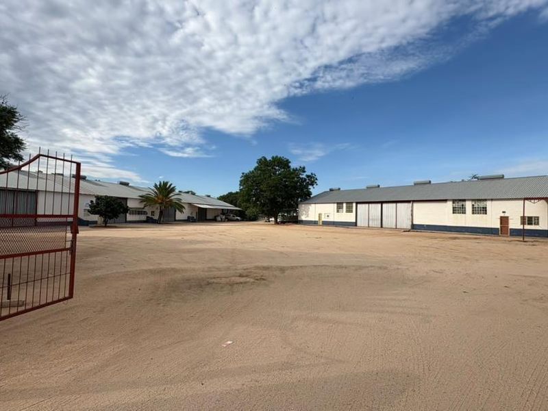 A wide-angle view of a commercial property featuring large warehouse structures with metal sliding doors and a spacious unpaved yard area.