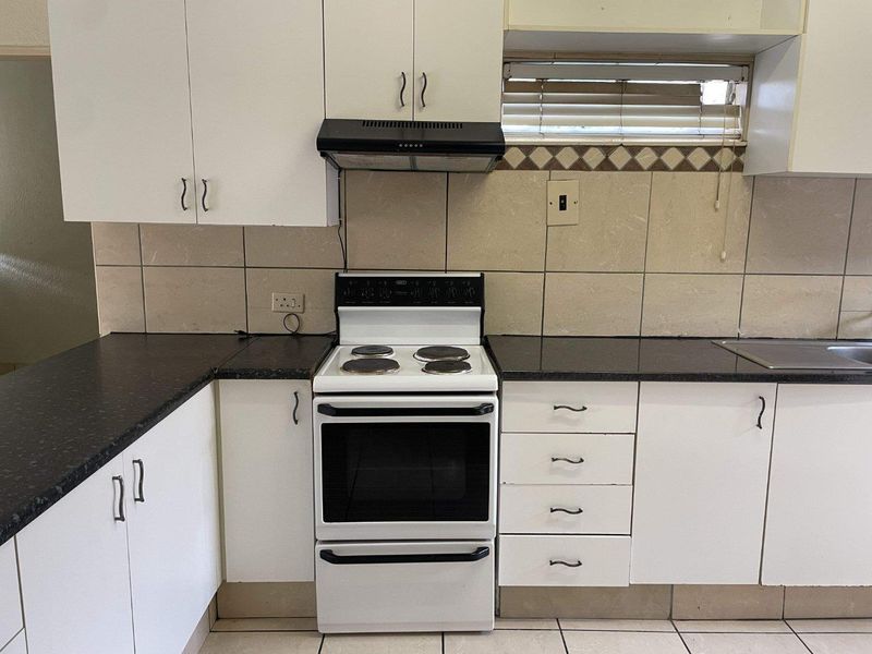 A functional kitchen featuring white cabinetry, dark laminate countertops, a freestanding electric stove with extractor fan, and tiled backsplash.