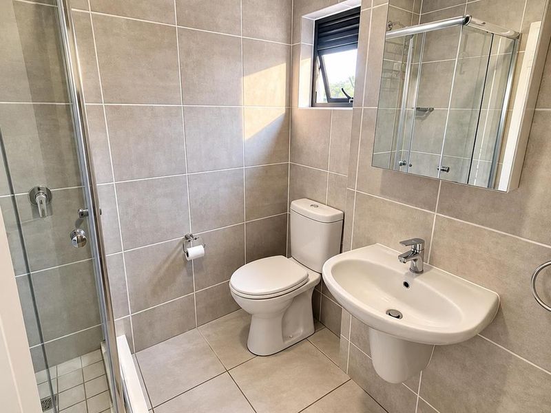 Modern bathroom featuring a glass shower enclosure, wall-mounted basin, toilet, and neutral floor-to-ceiling tiling with a functional mirror cabinet.