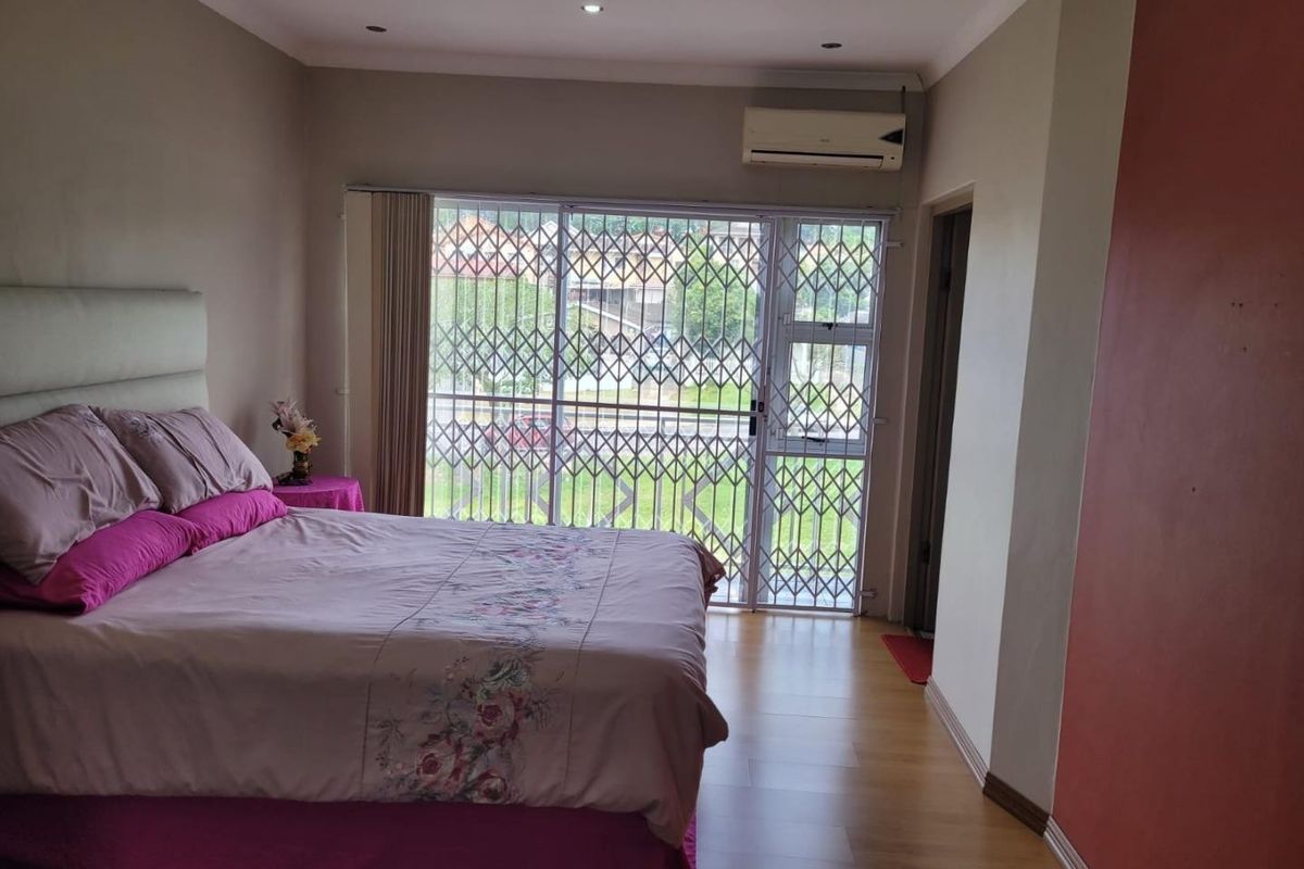 A bedroom featuring laminate flooring, recessed lighting, a wall-mounted air conditioning unit, and a sliding glass door with a security gate.
