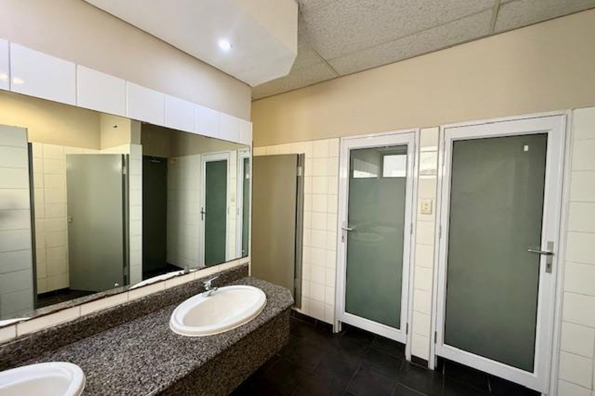 A functional office restroom featuring a granite vanity countertop, dual drop-in sinks, large wall-mounted mirror, and multiple private cubicle doors.