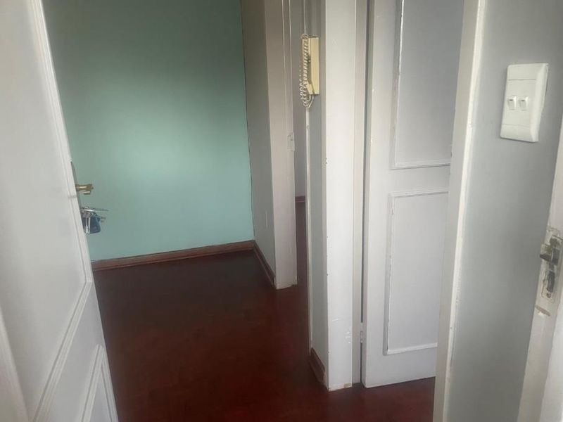 A functional hallway featuring timber flooring, panelled doors, and an integrated intercom system, providing access to adjacent rooms within the apartment.