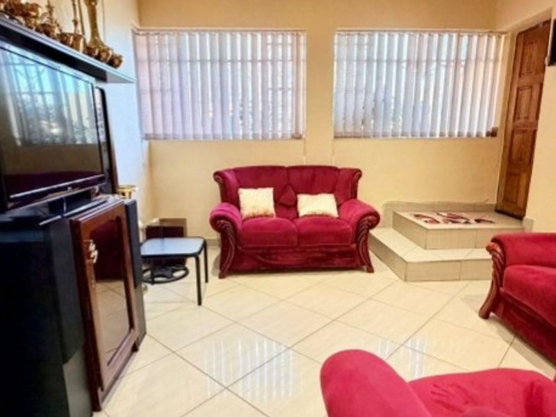 A living room featuring tiled flooring, vertical blinds, and a raised platform area, providing a functional space for relaxation.
