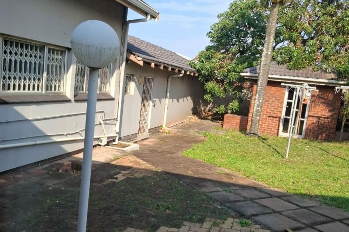 Rear exterior view featuring a paved courtyard, garden area, and a detached brick outbuilding with security features.