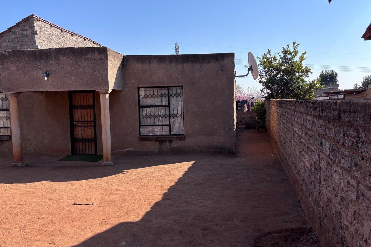 Rear exterior view of the house featuring a covered entrance, security bars on windows, and a surrounding brick boundary wall.