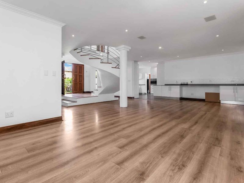 Spacious open-plan living area featuring modern laminate flooring, recessed lighting, a striking spiral staircase, and a sleek kitchen with built-in cabinetry.