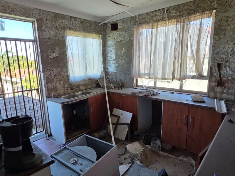 A kitchen in need of significant renovation, featuring existing cabinetry and sink, currently in a state of disrepair with damaged walls and ceiling.