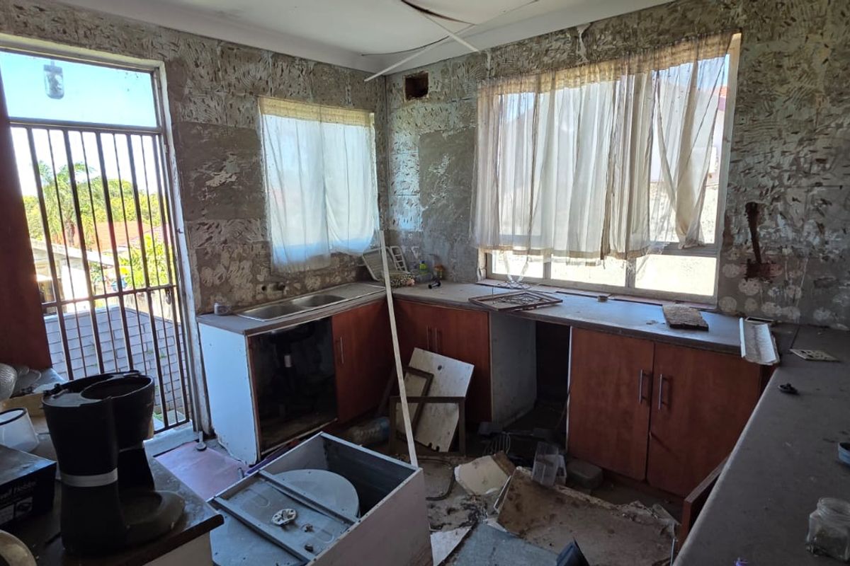 A kitchen in need of significant renovation, featuring existing cabinetry and sink, currently in a state of disrepair with damaged walls and ceiling.