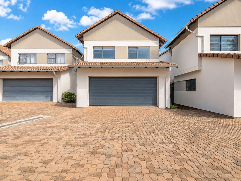Front elevation of a modern townhouse featuring a double garage, paved driveway, and tiled roof architecture.