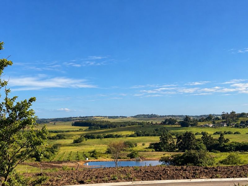 A scenic view overlooking rolling green hills, open fields, and a small pond on the residential land.