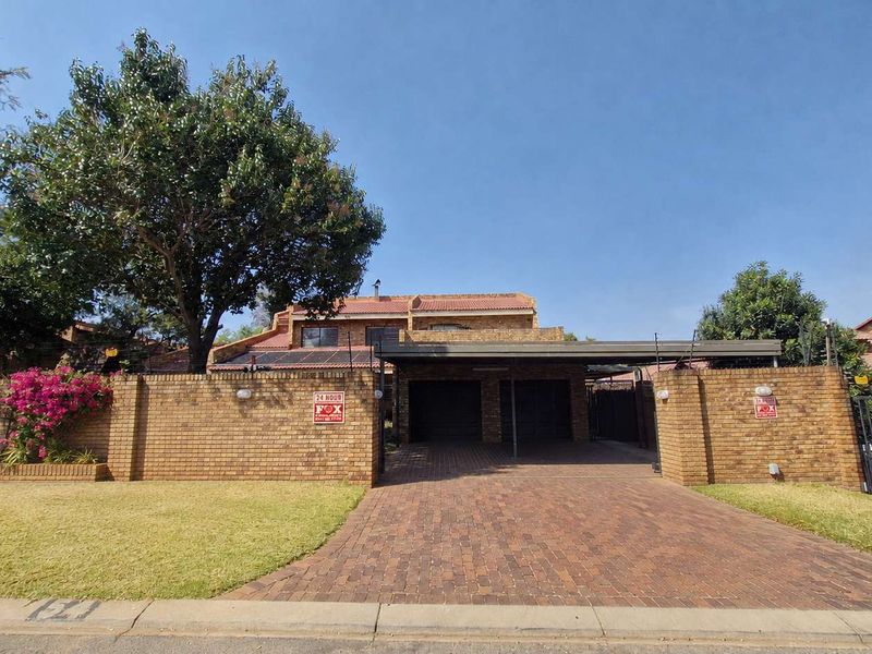 Front view of a brick-faced house featuring a paved driveway, double garage, carport, and secure boundary wall with electric fencing.