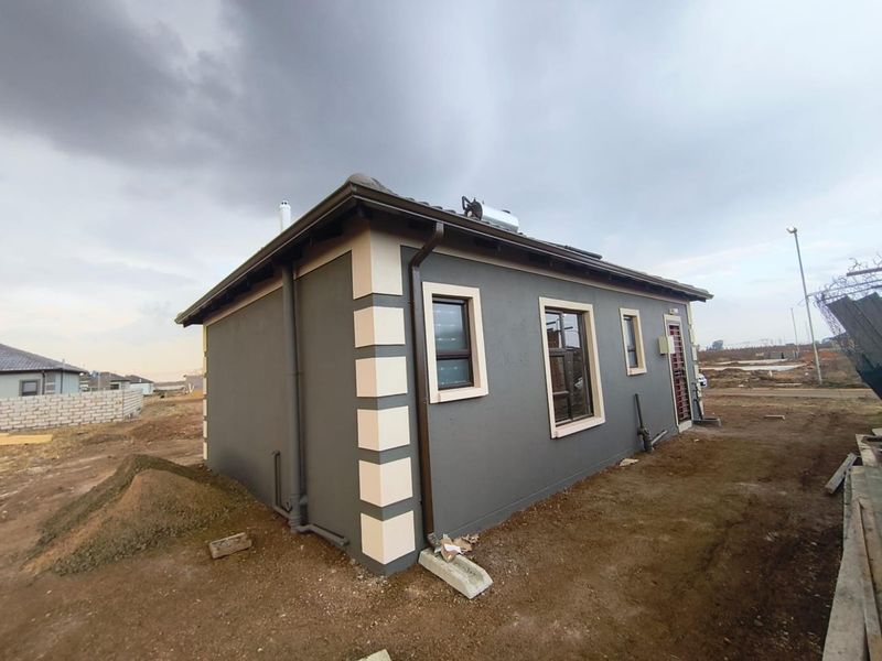 Rear view of a modern single-story house featuring dark grey exterior walls with contrasting quoins, solar geyser, and aluminium window frames.