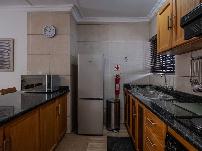 A functional kitchen featuring wooden cabinetry, granite countertops, a double sink, and integrated appliances with neutral tiled splashbacks.
