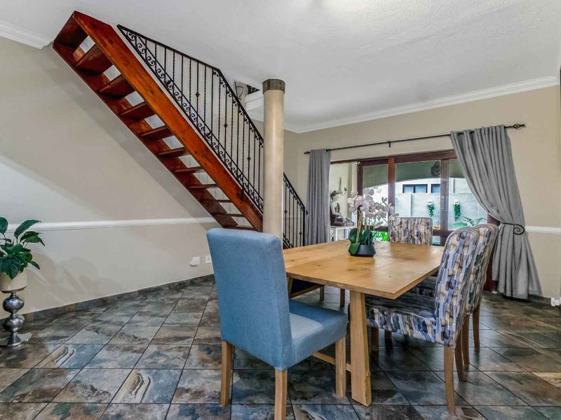 Dining area featuring stone tile flooring, a wooden staircase with wrought iron balustrade, and sliding glass doors leading to the outdoor space.