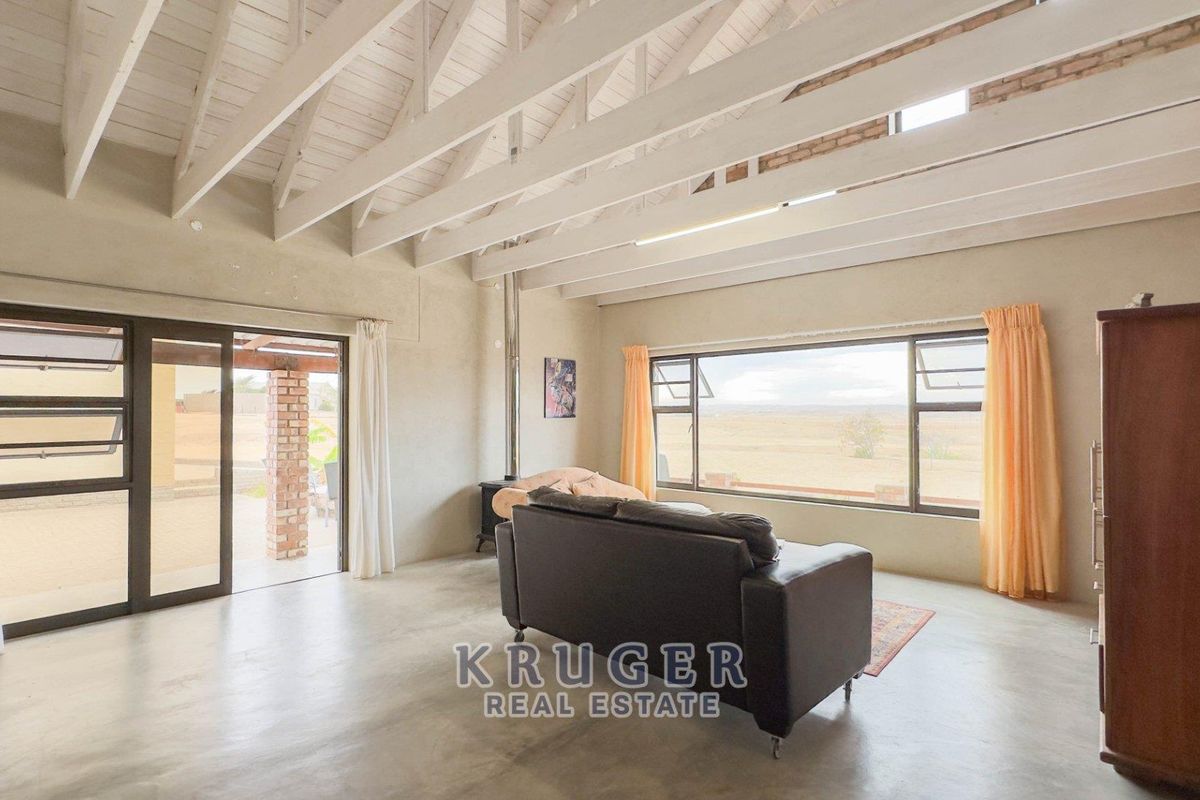 Spacious living area featuring high vaulted ceilings with exposed beams, large windows, and sliding doors leading to an outdoor patio.
