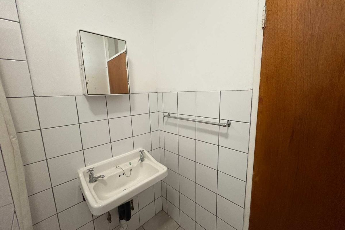 A dated bathroom featuring a wall-mounted basin, tiled splashback, and a medicine cabinet, requiring cosmetic updates to improve its overall condition.