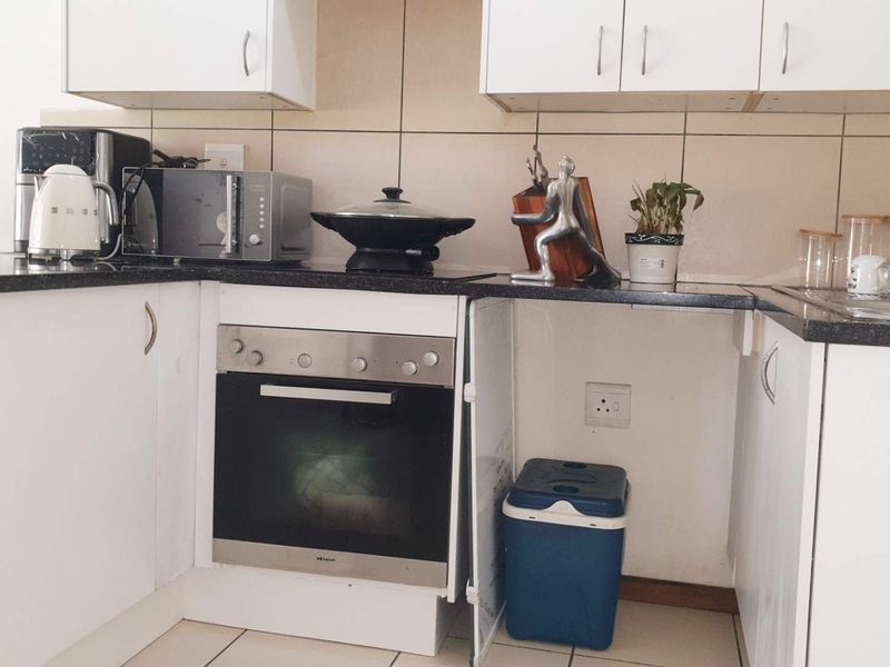 A compact kitchen featuring granite countertops, tiled backsplash, built-in oven, and white cabinetry, currently requiring minor repairs to the lower cabinet section.