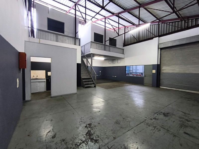 Spacious industrial warehouse unit featuring a mezzanine level, concrete flooring, roller shutter door access, and a small built-in kitchenette area.