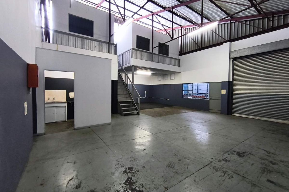 Spacious industrial warehouse unit featuring a mezzanine level, concrete flooring, roller shutter door access, and a small built-in kitchenette area.