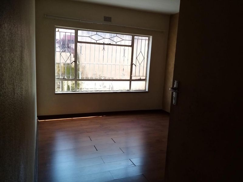 An empty bedroom featuring laminate flooring, a large window with security bars, and a ventilation grille, requiring minor repairs to the flooring.