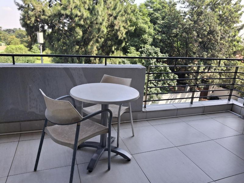 A private balcony featuring tiled flooring and a metal balustrade, offering an elevated outdoor space with views of surrounding trees.
