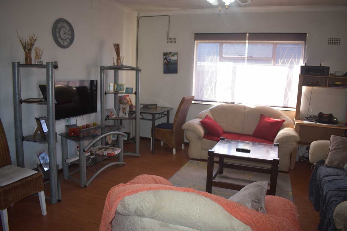 A living room featuring laminate flooring, a large window with security bars, and surface-mounted electrical wiring.