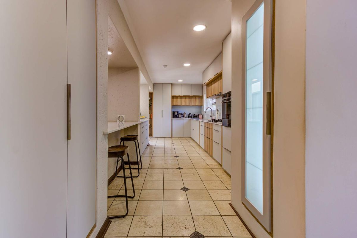 A modern galley-style kitchen featuring clean-lined cabinetry, a breakfast bar, integrated appliances, and neutral ceramic tile flooring with decorative accents.