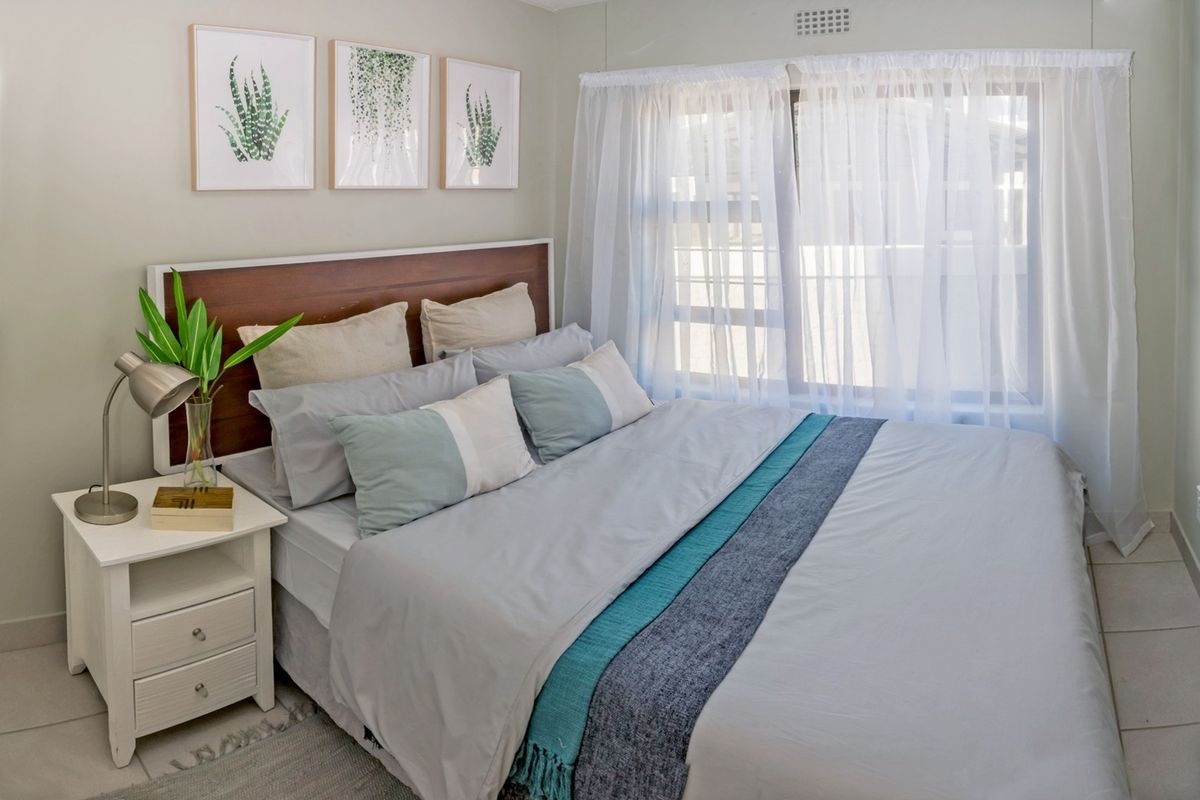 A well-maintained bedroom featuring tiled flooring, a built-in headboard, and natural light through a large window.