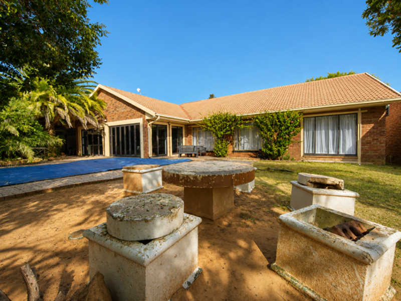 Rear view of a brick house featuring a swimming pool with cover, sliding glass doors, and a garden area with fixed concrete seating.
