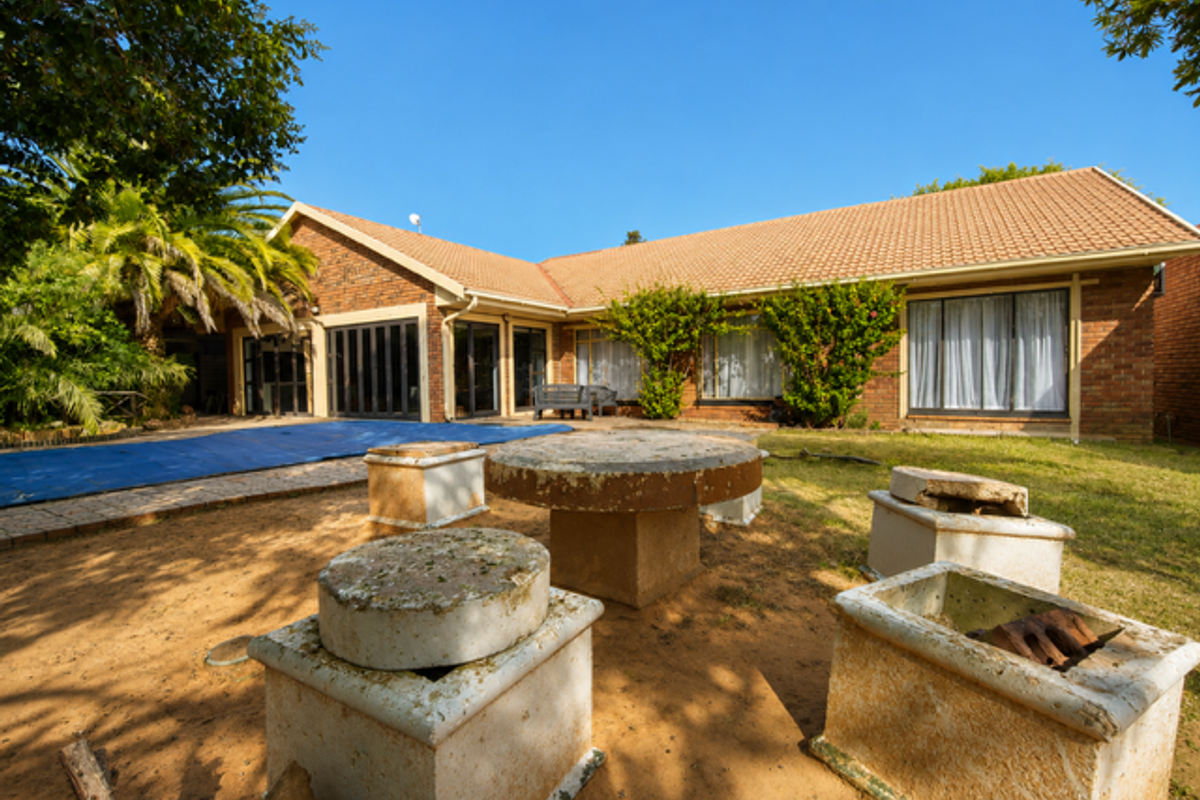 Rear view of a brick house featuring a swimming pool with cover, sliding glass doors, and a garden area with fixed concrete seating.