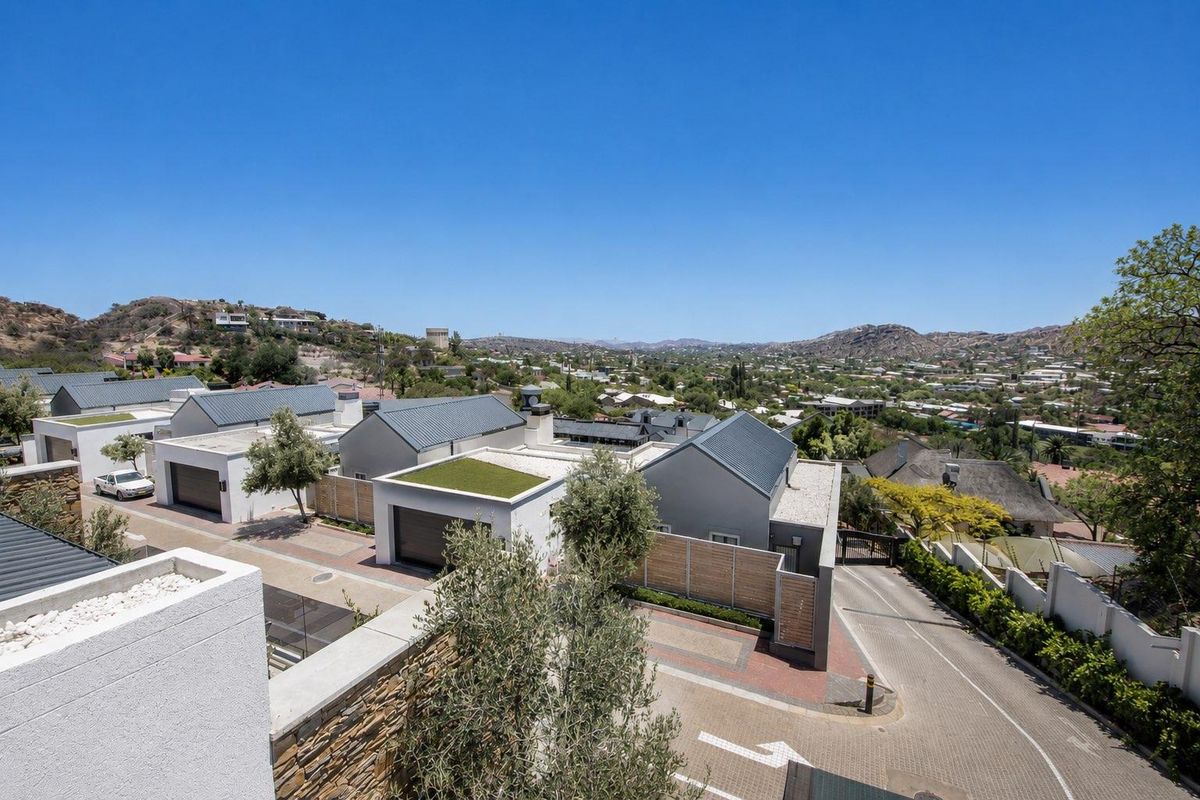 An elevated aerial view of a modern townhouse complex featuring paved driveways, metal roofing, and landscaped green roof sections.