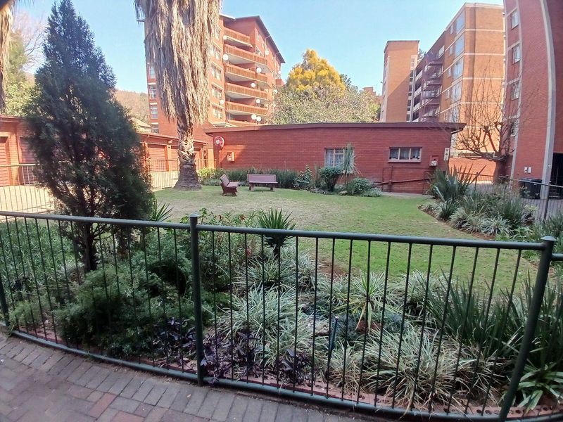 A view of a communal garden area featuring a lawn, established landscaping, and brick apartment building facades in the background.
