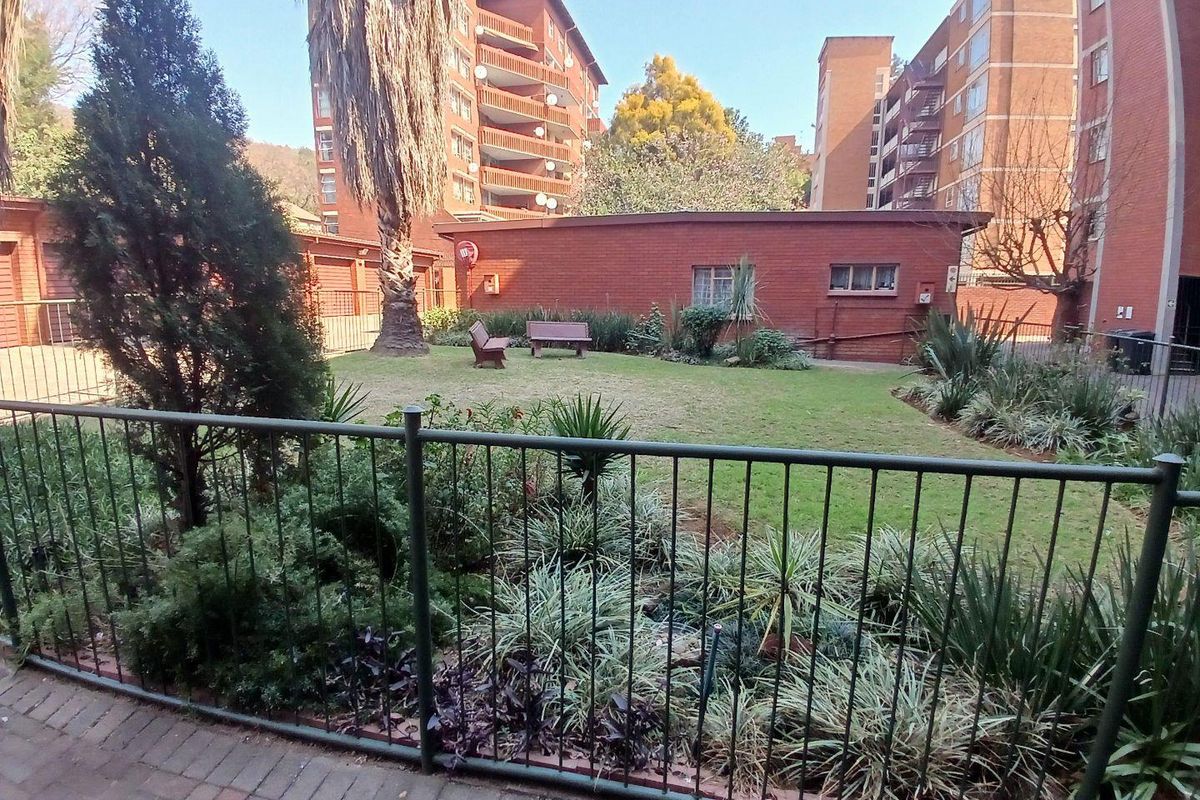 A view of a communal garden area featuring a lawn, established landscaping, and brick apartment building facades in the background.