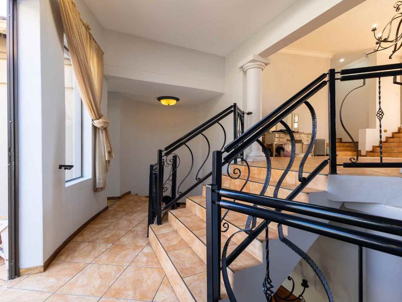 Spacious entrance hall featuring a tiled staircase with decorative wrought iron railings and a classic column architectural detail.